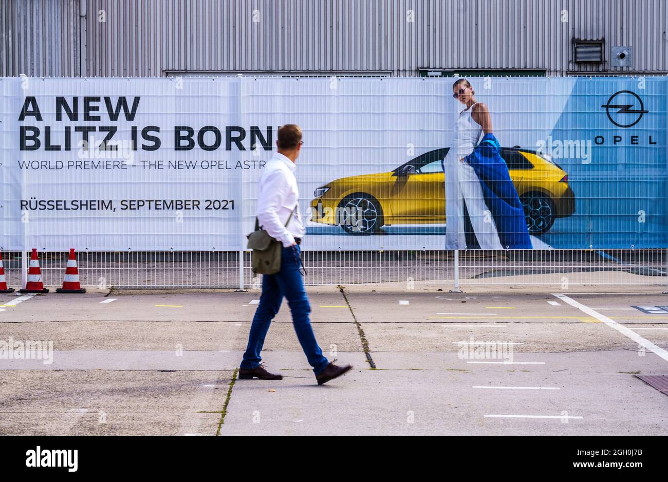 01. September 2021, Hessen, Rüsselsheim: Ein Mann geht an einem Banner vorbei, das für den neuen Opel Astra wirbt. Der Automobilhersteller Opel stellt seine sechste Generation des neuen Opel Astra vor. Die aktuelle Generation ist auch als Plug-in-Hybrid erhältlich und wird voraussichtlich Anfang 2022 geliefert. Foto: Andreas Arnold/dpa Stockfoto
