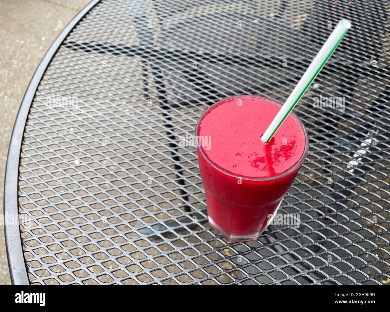 Ein klares Glas mit rotem Fruchtgetränk auf der Basis von Smoothie Bete, von oben betrachtet, mit Stroh.Sat auf einem kontrastierenden schwarzen Gitterwerk Stockfoto