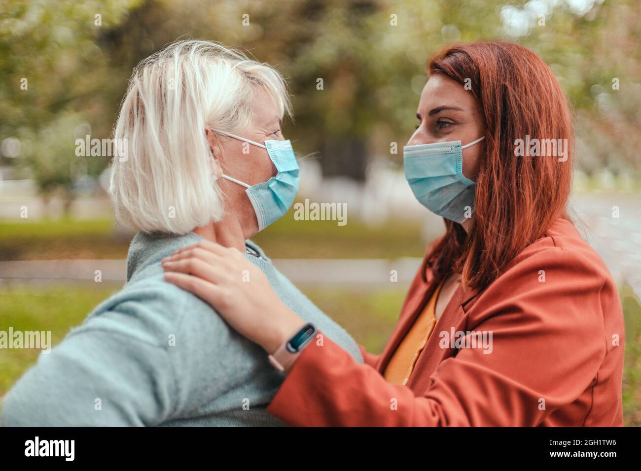 Liebe und Freundschaft Konzept. Familienumarmung Mutter und Tochter mit schützenden chirurgischen Gesichtsmasken umarmen sich im Park. Stockfoto
