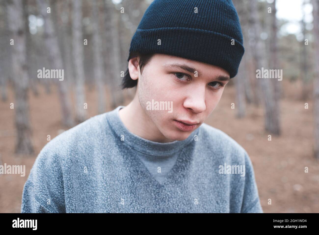 Der 16-17-jährige Teenager trägt Sweatshirt und Strickmütze, die in Wäldern posiert und die Kamera anschaut. Teenagerhood. Ernst Kerl posiert im Freien. Stockfoto