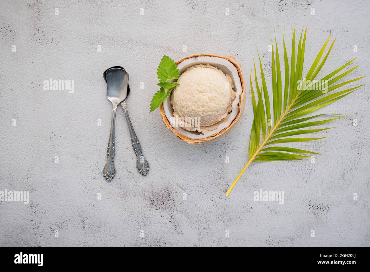 Kokoseis Aromen in der Hälfte der Kokosnuss Setup auf weißem Stein Hintergrund. Sommer und Süße Menükonzept. Stockfoto