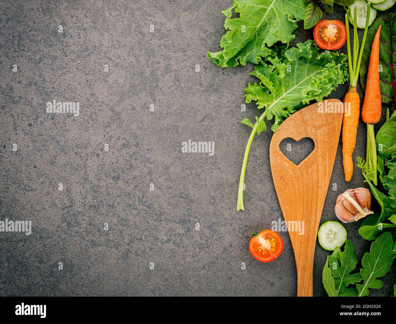 Holzlöffel und Gemüse auf dunklem Stein Hintergrund. Gesunde Ernährung und gesundes Kochen Konzept. Stockfoto