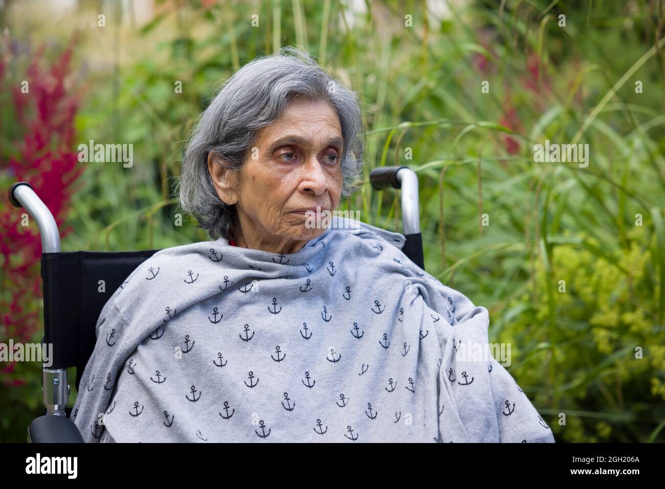 Eine alte Frau, britisch-asiatische Inderin, die im Rollstuhl sitzt und traurig und besorgt aussieht. Großbritannien psychische Gesundheit Konzept, Depressionen, Gesundheitsversorgung und Pflege für die Stockfoto