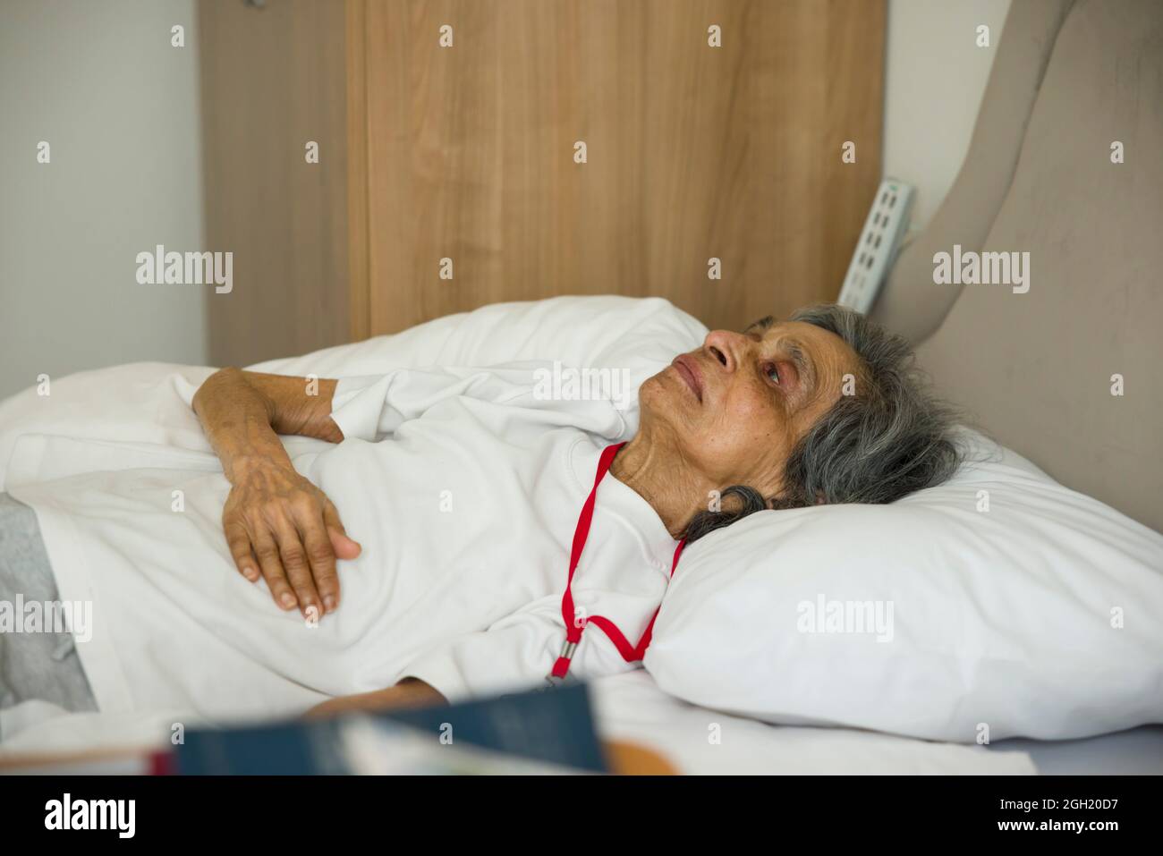 Gebrechliche alte indisch-asiatische Frau, die im Bett in einem Krankenhauszimmer oder Pflegeheim, Großbritannien, liegt. Stockfoto