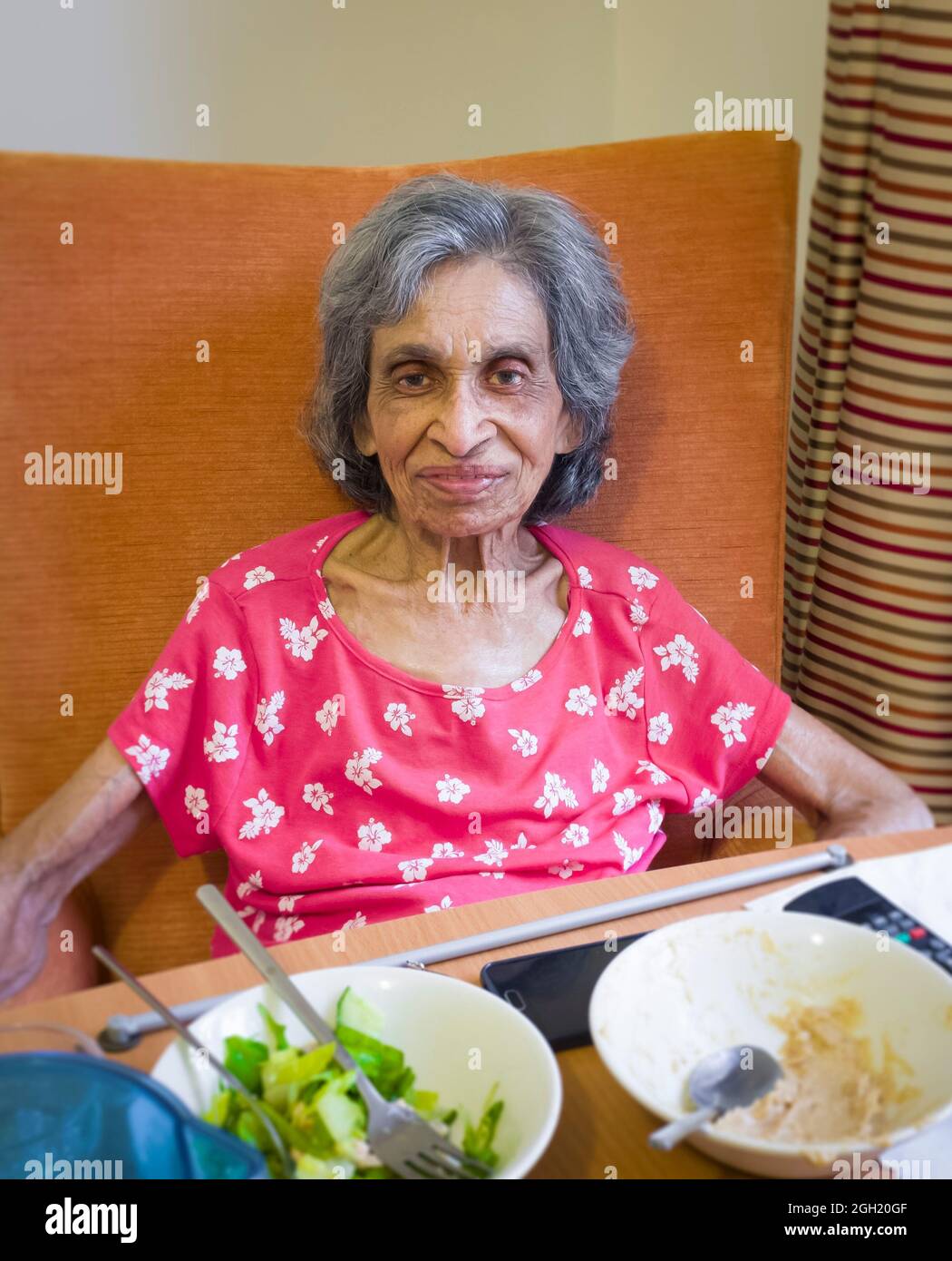 Ältere indische Frau in einem Pflegeheim oder Pflegeheim, Großbritannien, sitzt auf einem Stuhl und isst eine Mahlzeit. Zeigt Gebrechlichkeit und Unterernährung im Alter Stockfoto