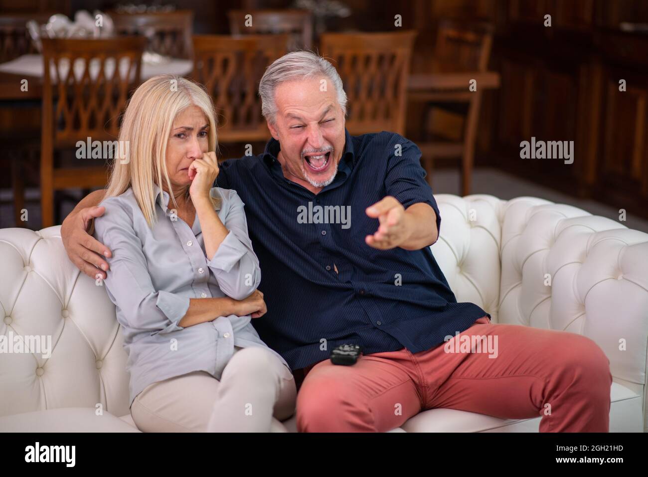 Mann, der ein gutes Lachen hat, seine Frau weint, während sie das gleiche fernsehprogramm ansieht, mangelndes Empathie-Konzept Stockfoto