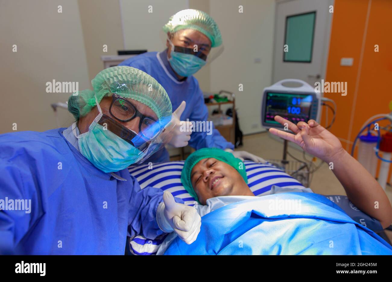 Team von Chirurgen Ärzte und wiedergewonnen Patienten glücklich und heben die Hände für Daumen nach oben und zeigen Siegeszeichen nach Abschluss und Erfolg in der Operation Stockfoto