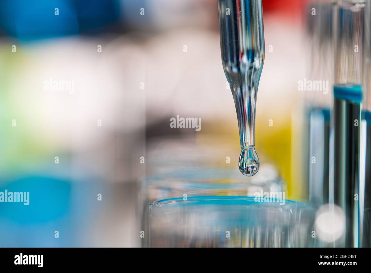 Tropfen blauer Flüssigkeit vom Tropfen zum Reagenzglas im Labor mit heller Farbunschärfe im Hintergrund. Konzept des reinen und sauberen Extrakts. Stockfoto