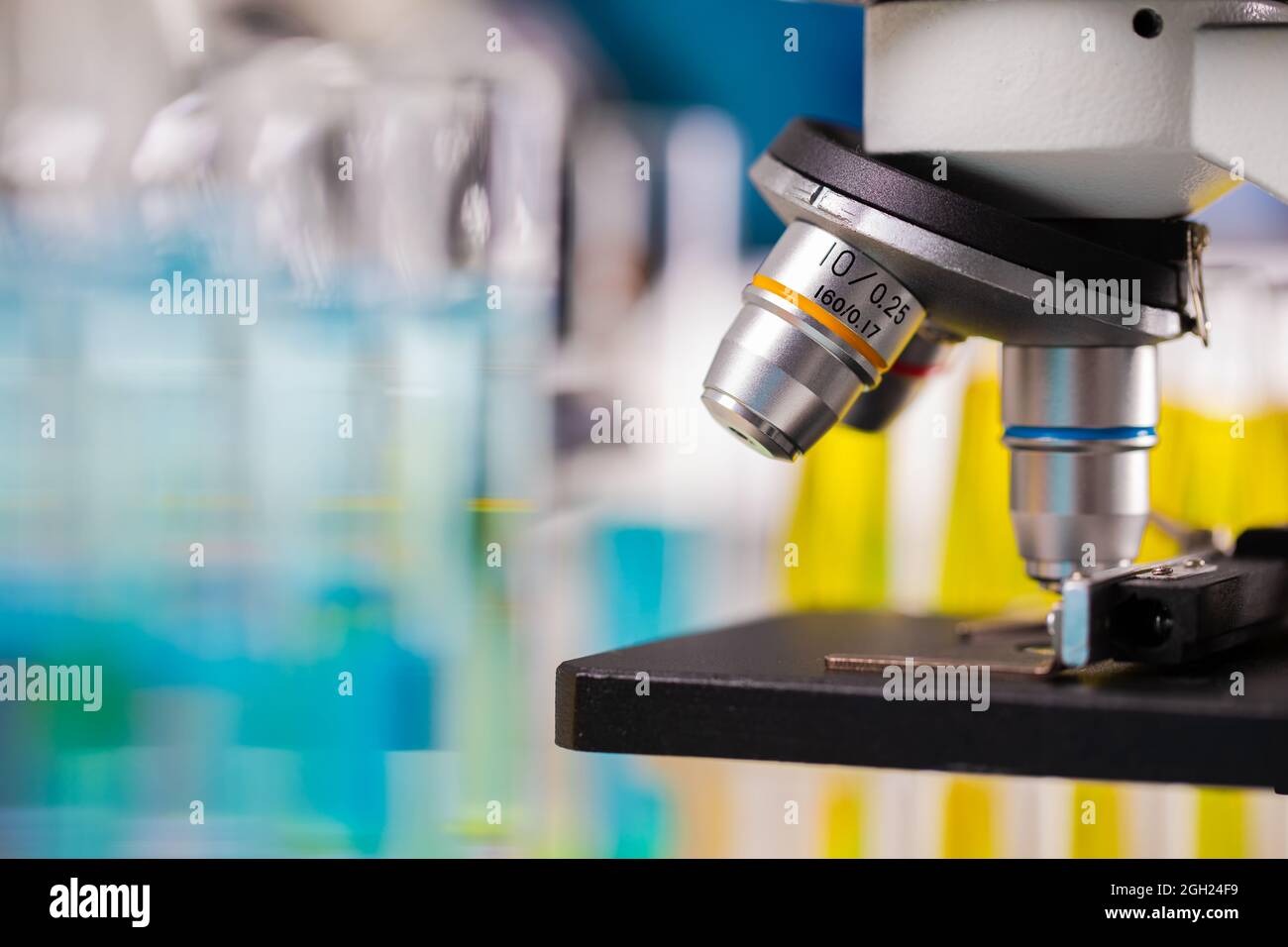 Nahaufnahme des Mikroskopobjektivs mit verwacklungsfarbigem Hintergrund von Reagenzgläsern und Bechergläsern, die Platz kopieren. Stockfoto