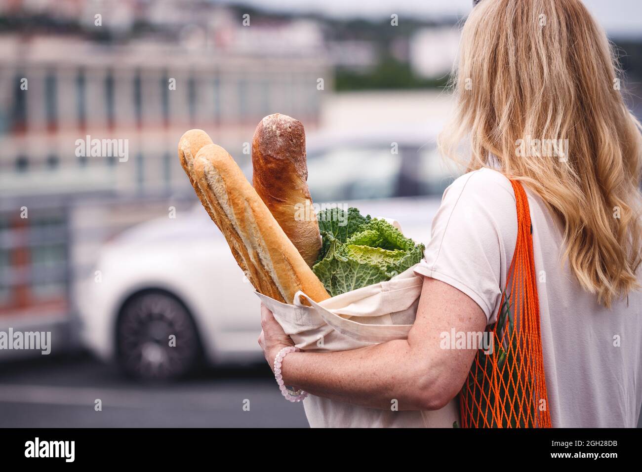 Frau mit Lebensmitteln geht auf einem Supermarkt-Parkplatz zu ihrem Auto. Kunden mit wiederverwendbaren Taschen ehren einen nachhaltigen Lebensstil ohne Abfall Stockfoto
