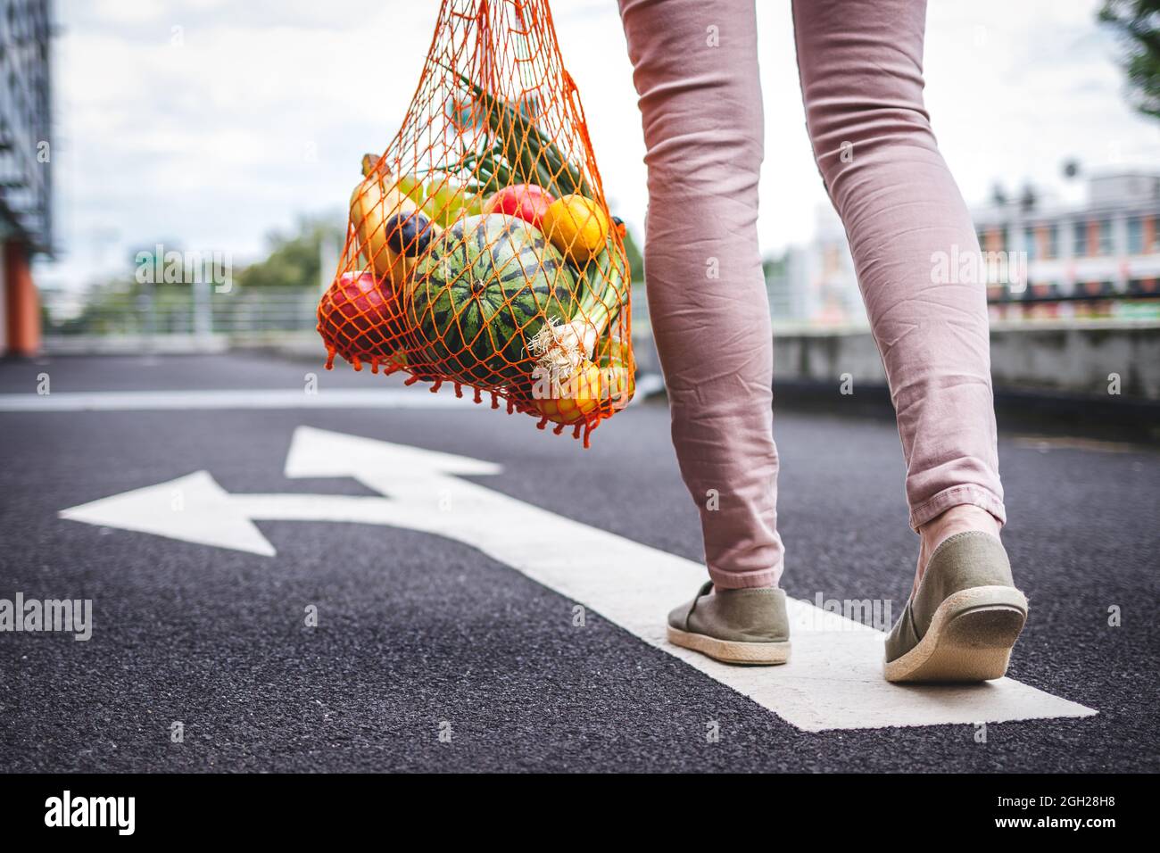 Wählen Sie die richtige Richtung für einen gesunden und nachhaltigen Lebensstil ohne Verschwendung. Frau mit wiederverwendbarem Netzbeutel voller Obst unterwegs Stockfoto