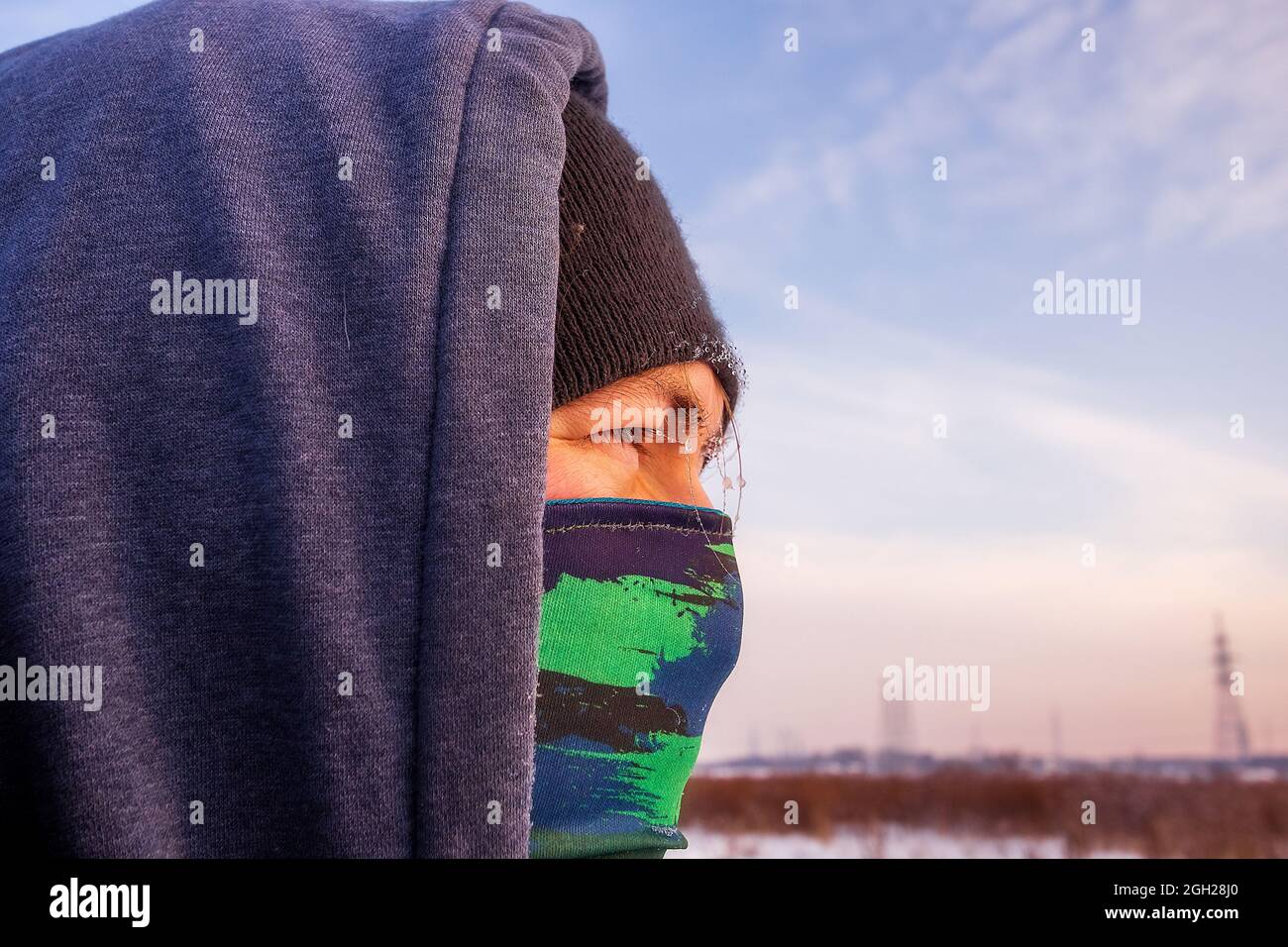 Nahaufnahme eines kaukasischen Mannes mit einem Schal als Maske und einer Winterjacke mit Kapuze. Stockfoto