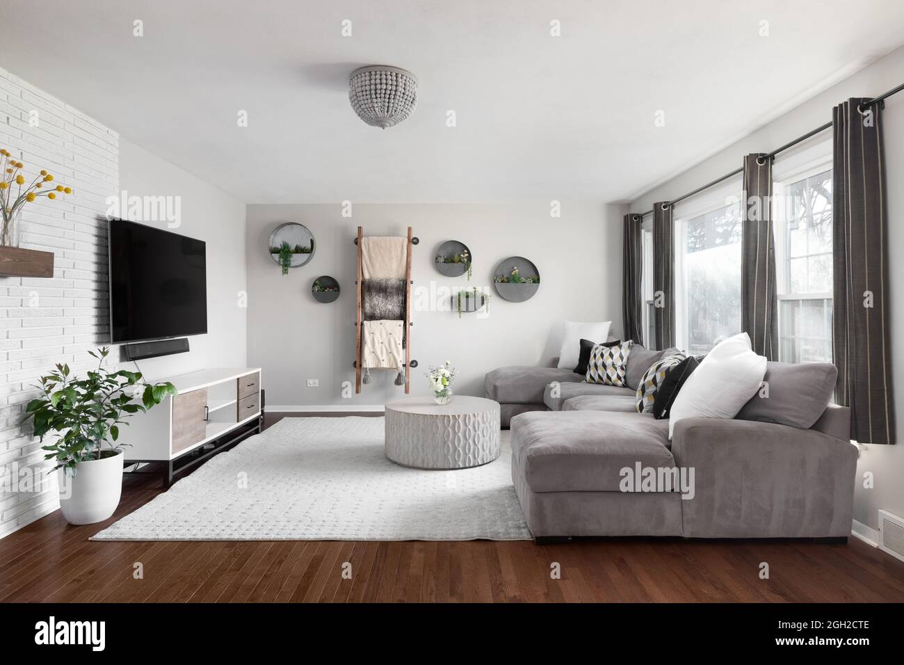 Ein wunderschönes, gemütliches Wohnzimmer mit einer weißen Ziegelwand, einem Fernseher, Blumentöpfen an der Wand und einer Couch. Stockfoto