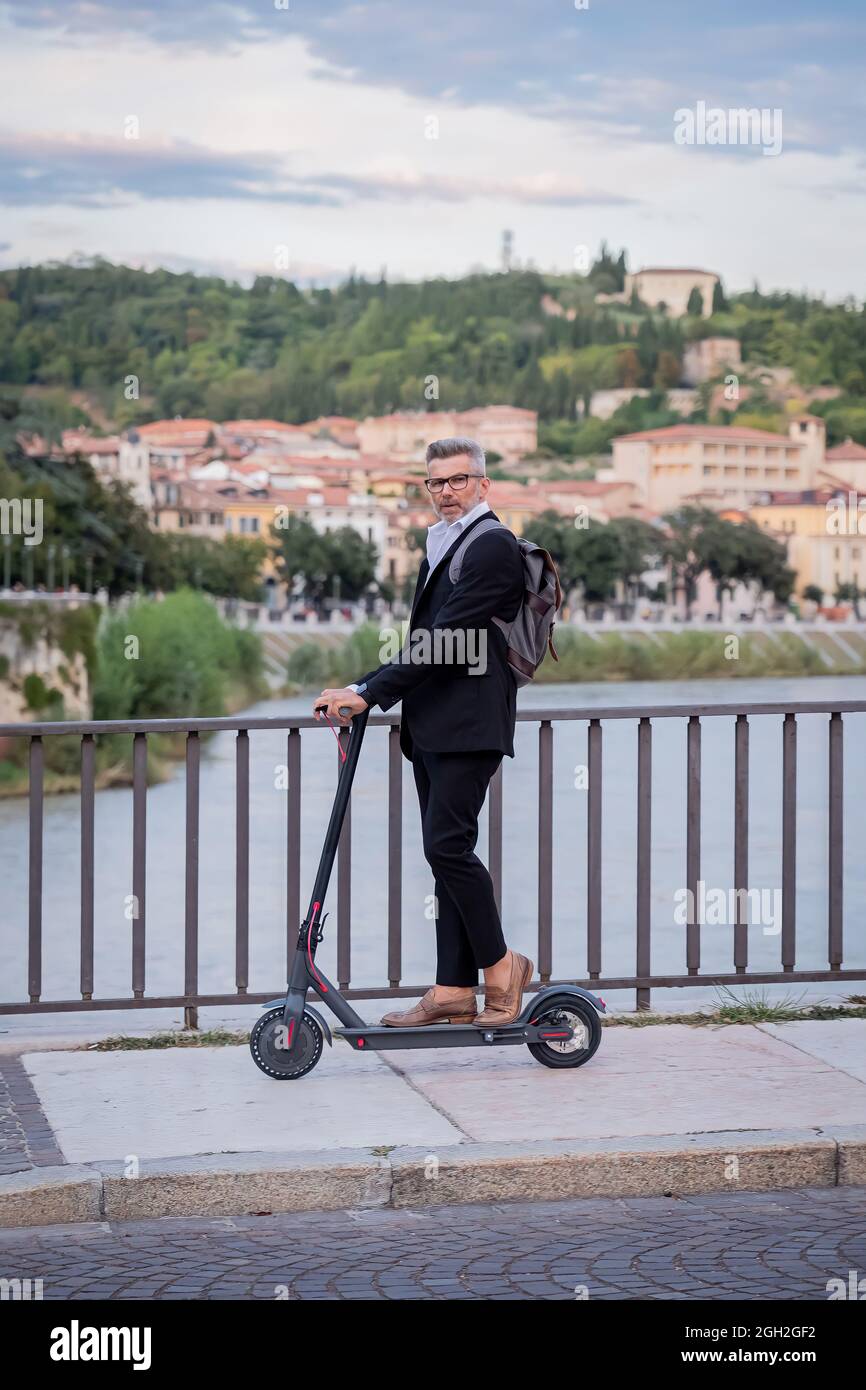 Schöner Geschäftsmann in Anzug Reiten eines Elektrorollers, während pendeln in der Stadt zu arbeiten. Ökologisches Transportkonzept Stockfoto