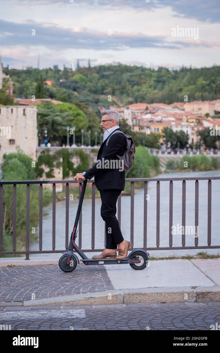 Schöner Geschäftsmann in Anzug Reiten eines Elektrorollers, während pendeln in der Stadt zu arbeiten. Ökologisches Transportkonzept Stockfoto