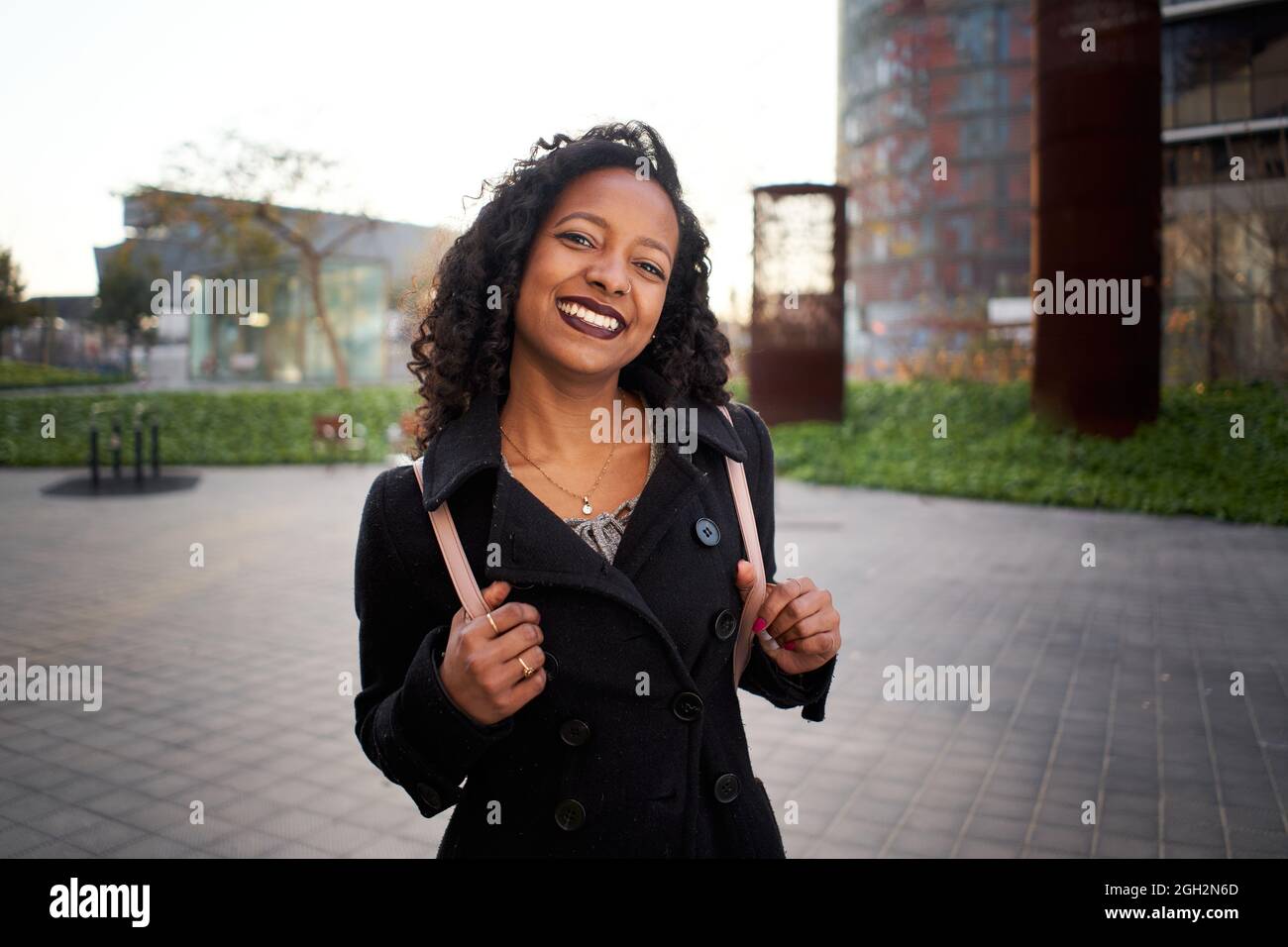 Die Geschäftsfrau von Latina lächelt fröhlich und schaut auf die Kamera. Die junge Frau steht neben einem modernen Bürogebäude in der Stadt. Sie trägt einen Stockfoto