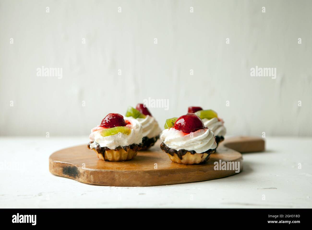 Cupcakes mit Quark auf Vintage-Tablett-leckerer Muffin mit Erdbeere und Kiwi auf Holzplatte Stockfoto