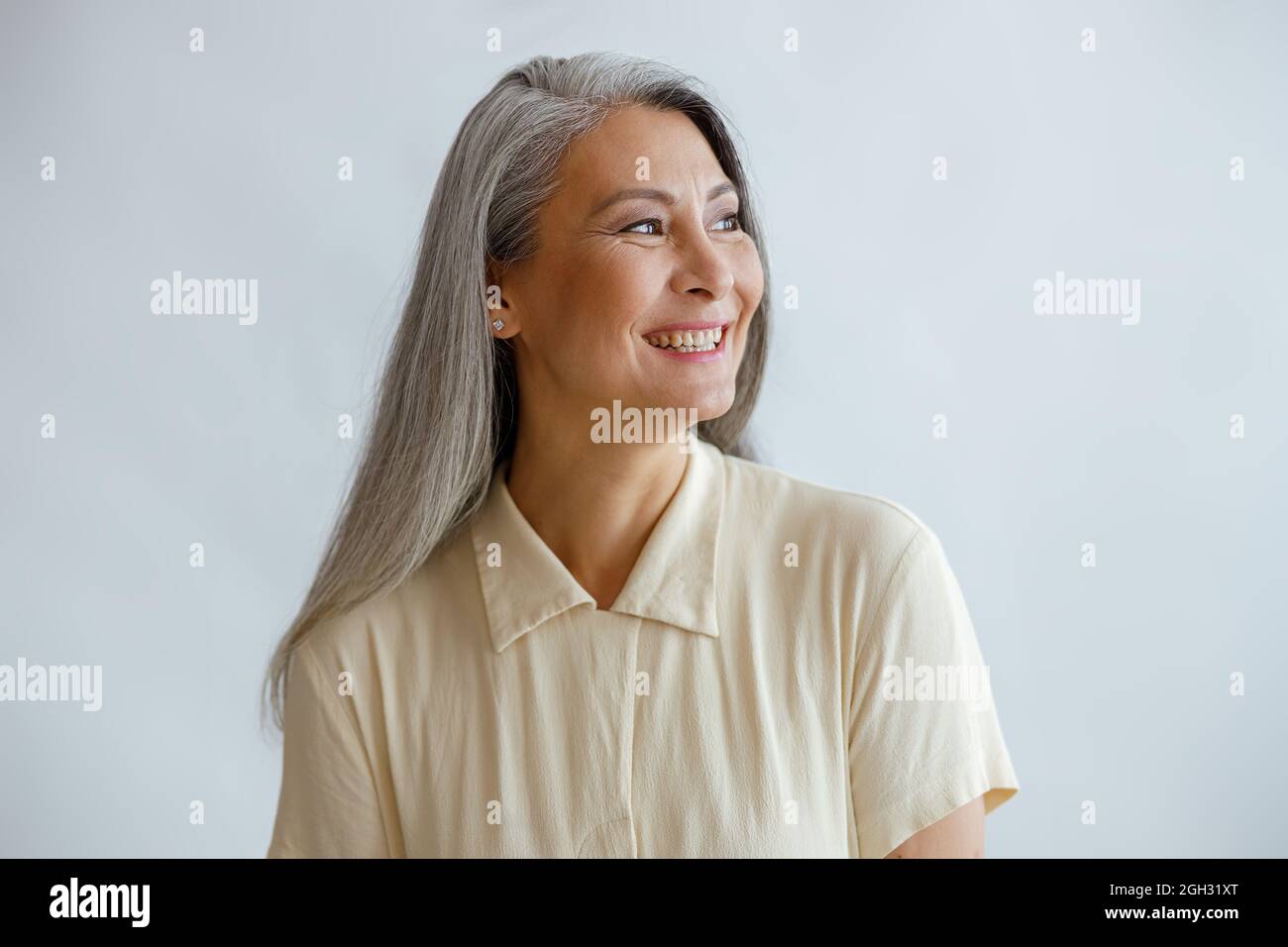 Fröhliche Dame mittleren Alters trägt beige Bluse steht auf hellem Hintergrund Stockfoto