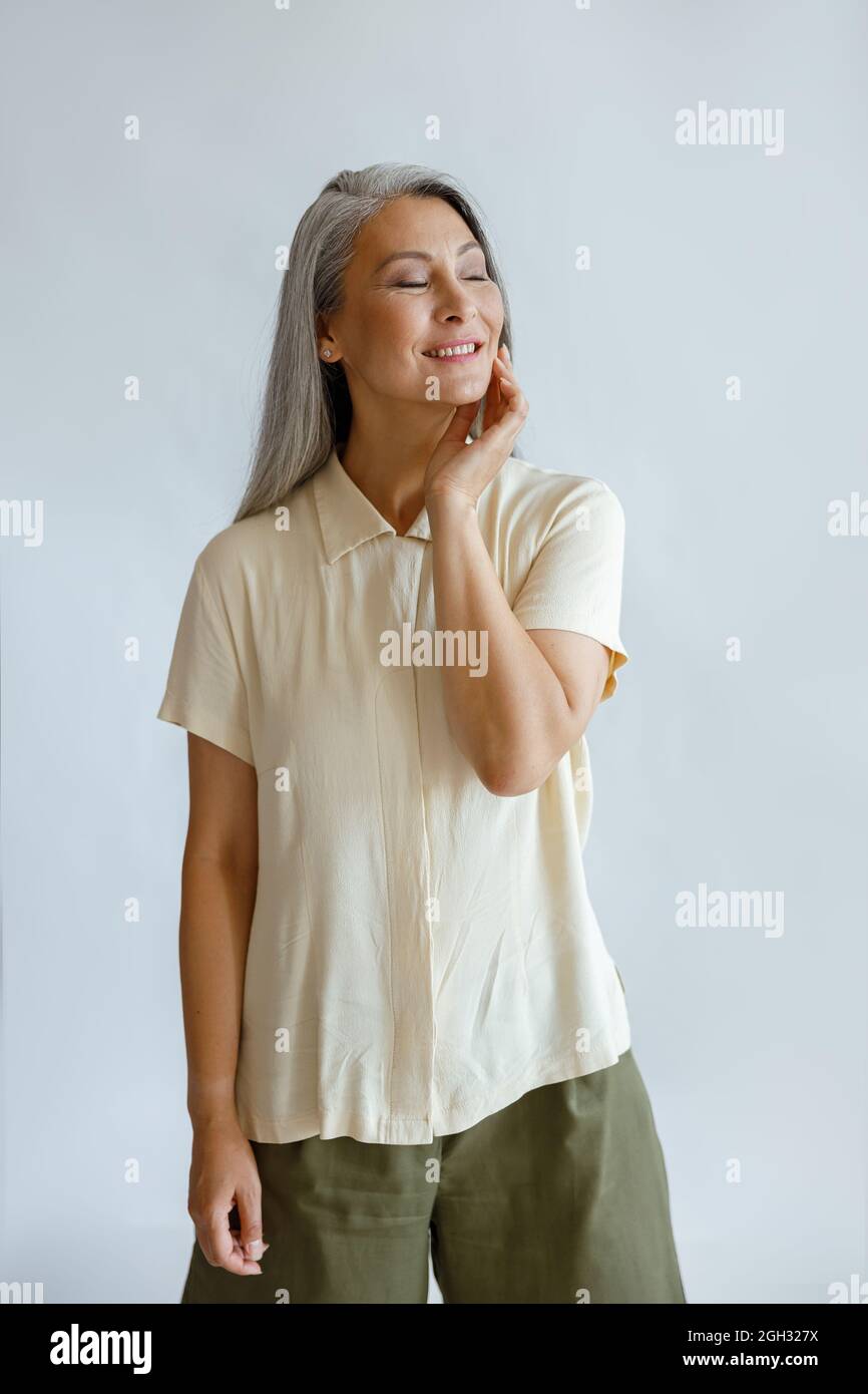 Fröhliche Mittelfrau in stilvoller Freizeitkleidung steht auf hellgrauem Hintergrund Stockfoto