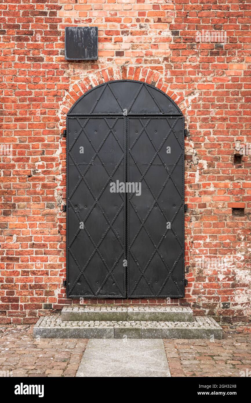 Eiserne Tür in einer roten Backsteinmauer. Gotische Burg der pommerschen Herzöge in Darłowo, Polen. Stockfoto