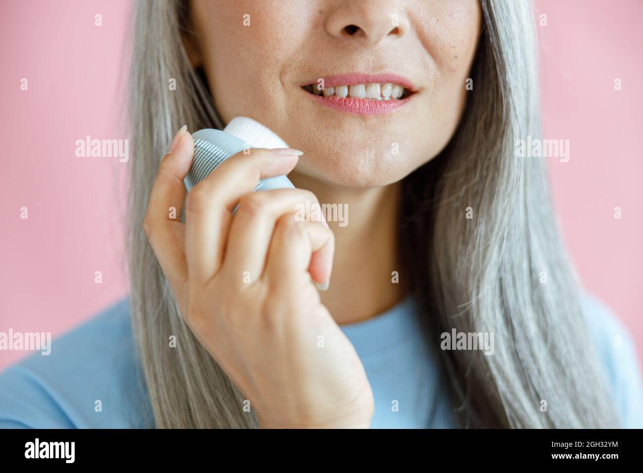 Glückliche Frau mittleren Alters reinigt Gesicht mit Sonic Bürste auf rosa Hintergrund stehen Stockfoto