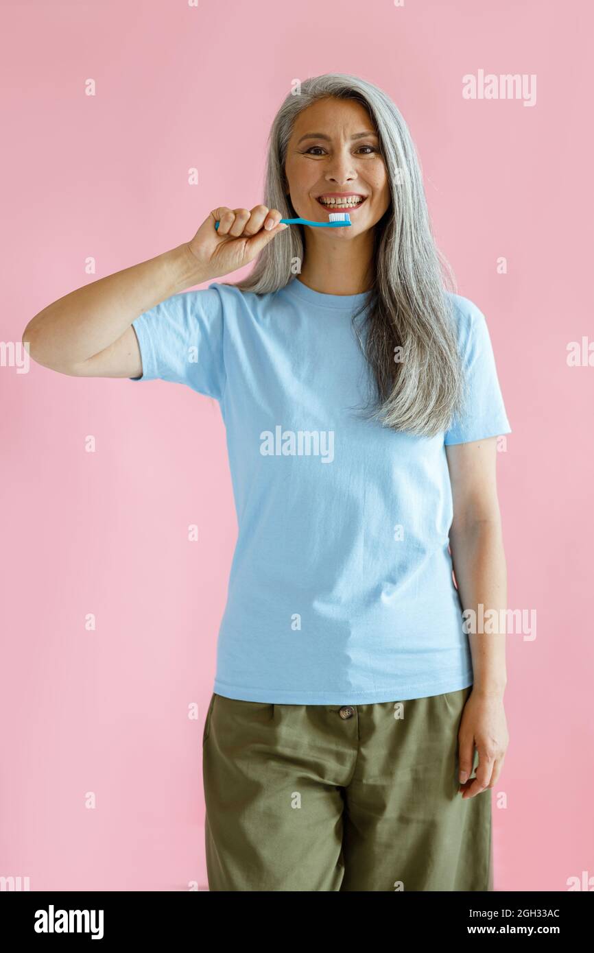 Positive langhaarige reifen asiatischen Modell hält Zahnbürste auf rosa Hintergrund Stockfoto