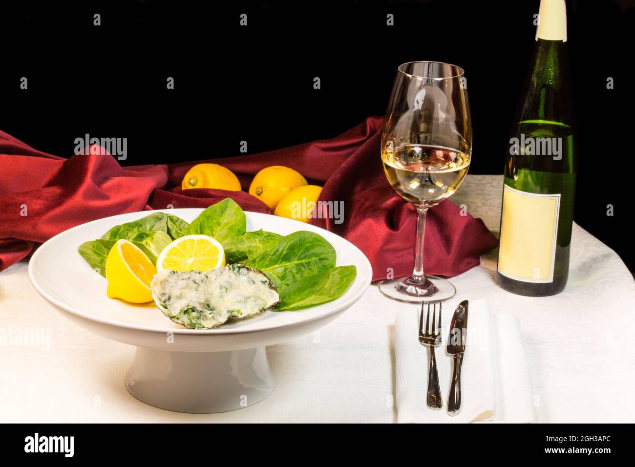 Gebackene Auster mit Spinat und Sahnesauce in Komposition mit Wein und Zitronen Stockfoto