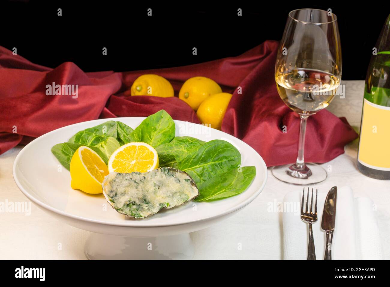 Gebackene Auster mit Spinat und Sahnesauce in Komposition mit Wein und Zitronen Stockfoto