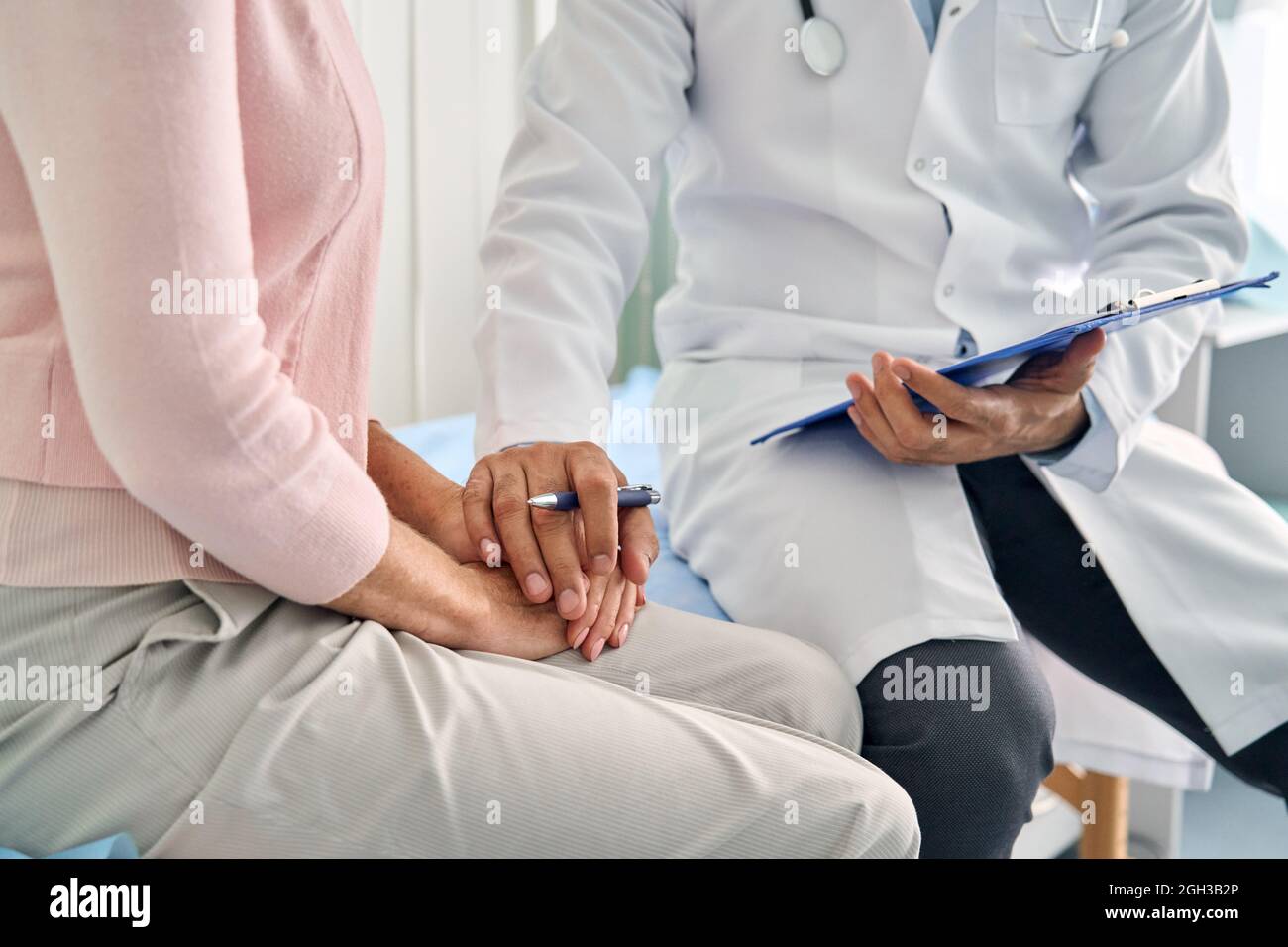 Männlicher Arzt, der ältere ältere weibliche Patientin mit der Hand konsultiert. Stockfoto