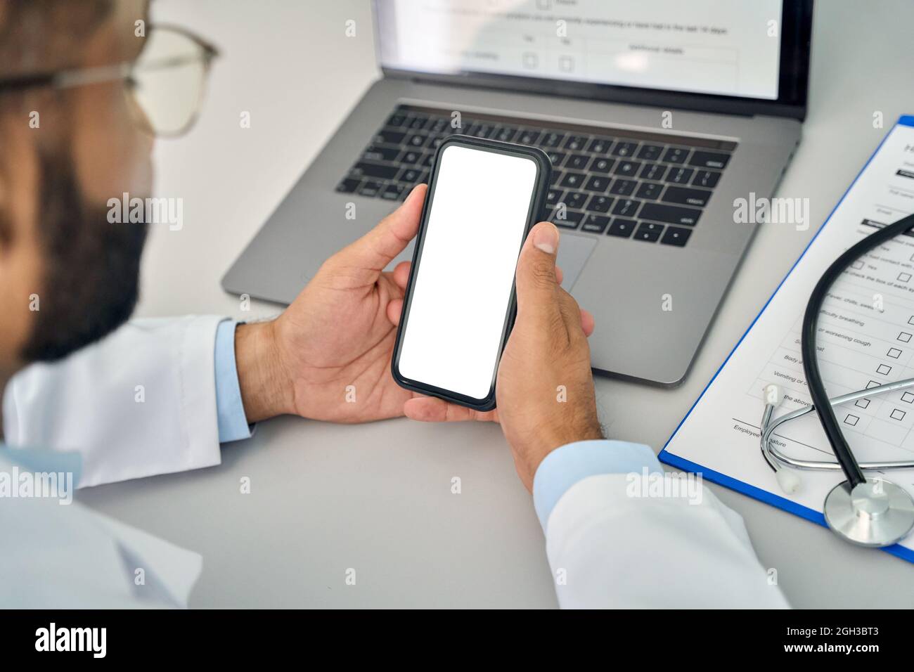Männlicher Arzt hält Mobiltelefon in den Händen und schaut auf den weißen Mockup-Bildschirm. Stockfoto
