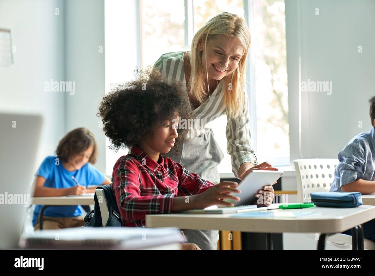 Lehrerin hilft afrikanischem Schulmädchen mit Tablet in der Klasse im Klassenzimmer. Stockfoto