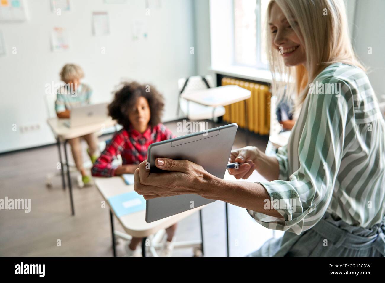 Lehrer, der Schüler in der Klasse mit einem digitalen Tablet im Klassenzimmer unterrichtet. Stockfoto
