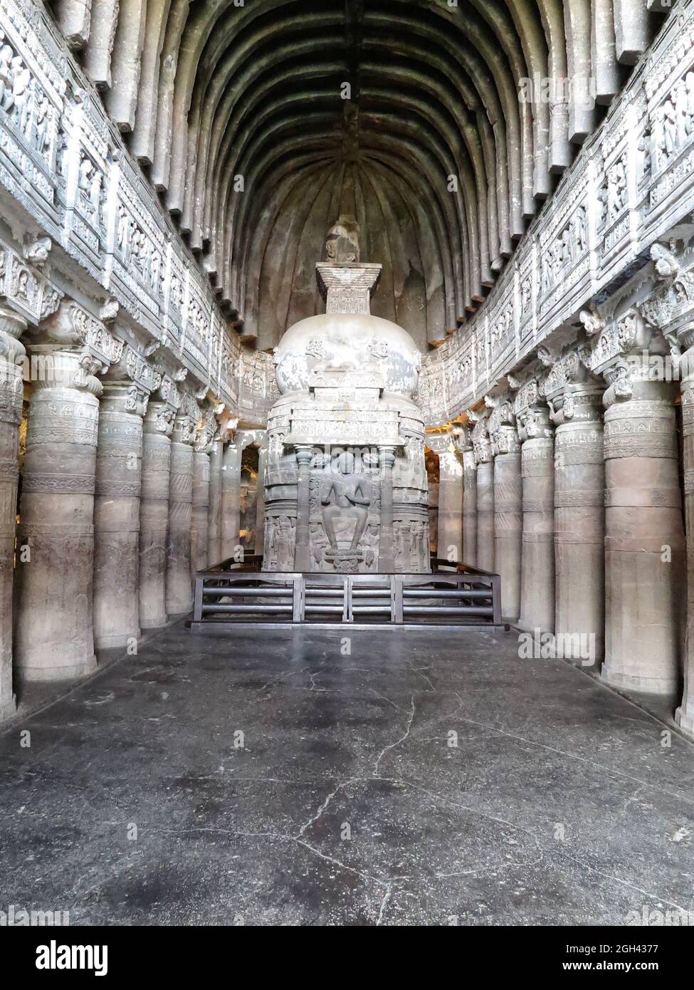 Verzierte Säulen und gewölbte Decke in Chaitya (Schrein) Halle mit großer Schnitzerei von sitzenden Buddha, Ajanta Cave 26, Maharashtra, Indien Stockfoto