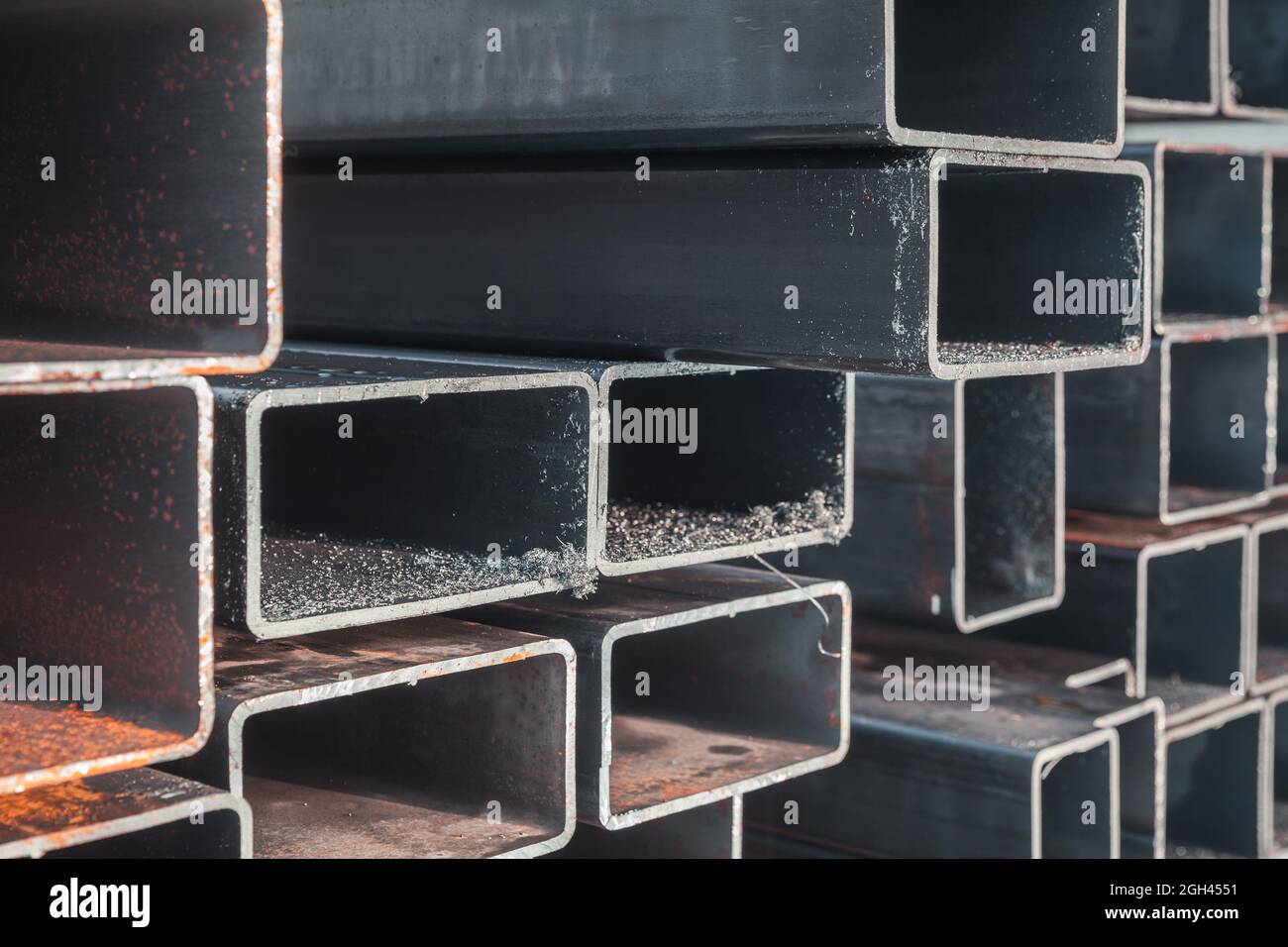 Abstrakter Hintergrund der Schwerindustrie. Stapel von gewalzten Stahlprodukten, Metallrohren mit rechteckigem Querschnitt, Nahaufnahme mit selektivem Fokus Stockfoto