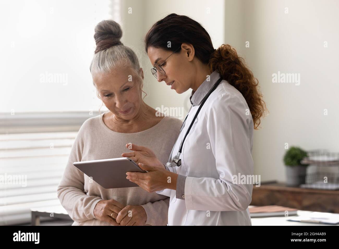 Ernsthafter Hausarzt, der alten weiblichen Patienten einen Tablet-Bildschirm zeigt Stockfoto