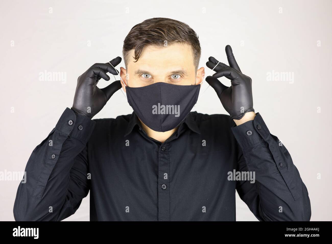 Ein Mann mit schwarzen medizinischen Handschuhen entfernt eine Schutzmaske Stockfoto