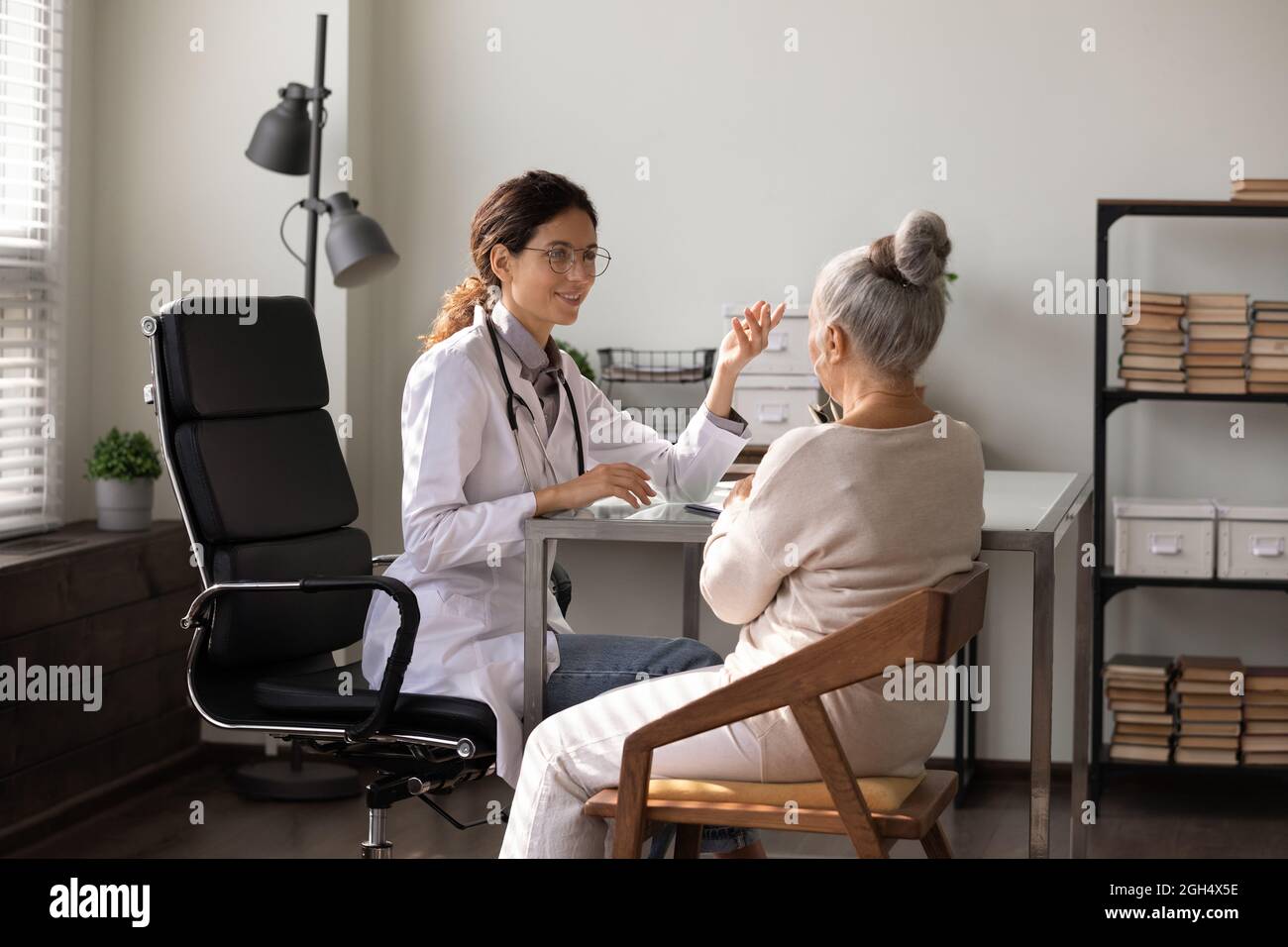 Lächelnder junger Arzt, der Ratschläge gibt und mit einer älteren Frau spricht Stockfoto