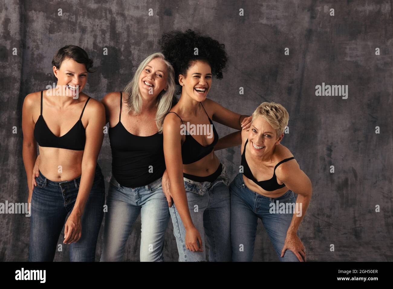 Verschiedene Frauen haben Spaß beim Tragen von Jeans und BHs. Vier körperpositive Frauen jeden Alters lächeln fröhlich und feiern ihre natürlichen Körper ag Stockfoto
