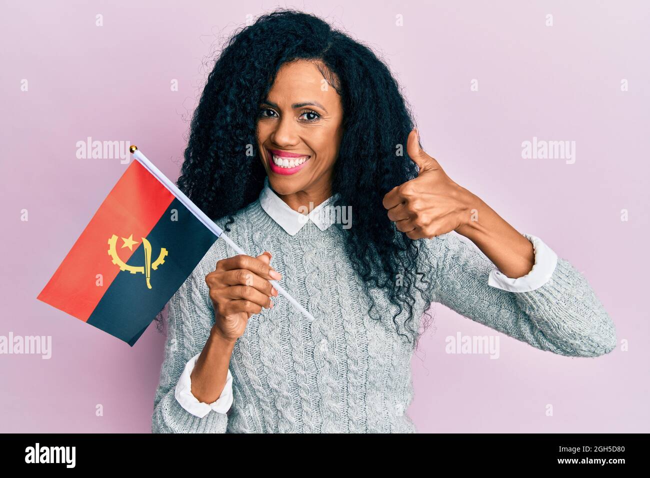 Eine afroamerikanische Frau mittleren Alters, die die angola-Flagge hält, lächelt glücklich und positiv, tut einen Daumen hoch und tut ein ausgezeichnetes und positives Zeichen Stockfoto