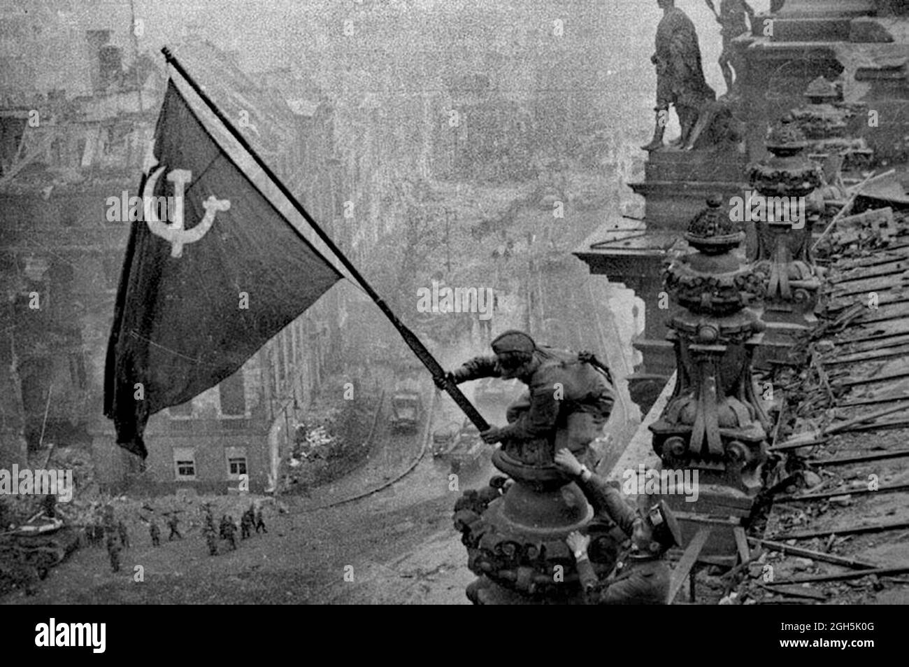 Ein sowjetischer Soldat, der die kommunistische Rote Flagge auf dem Reichstag in Berlin aufhebt, April 1945. Dies ist das ungedoktorte Foto - die Männer haben eine Uhr an jedem Handgelenk. In späteren Versionen, die von der sowjetischen Regierung zensiert wurden, wurden diese gestohlenen Uhren vom Foto entfernt. Stockfoto