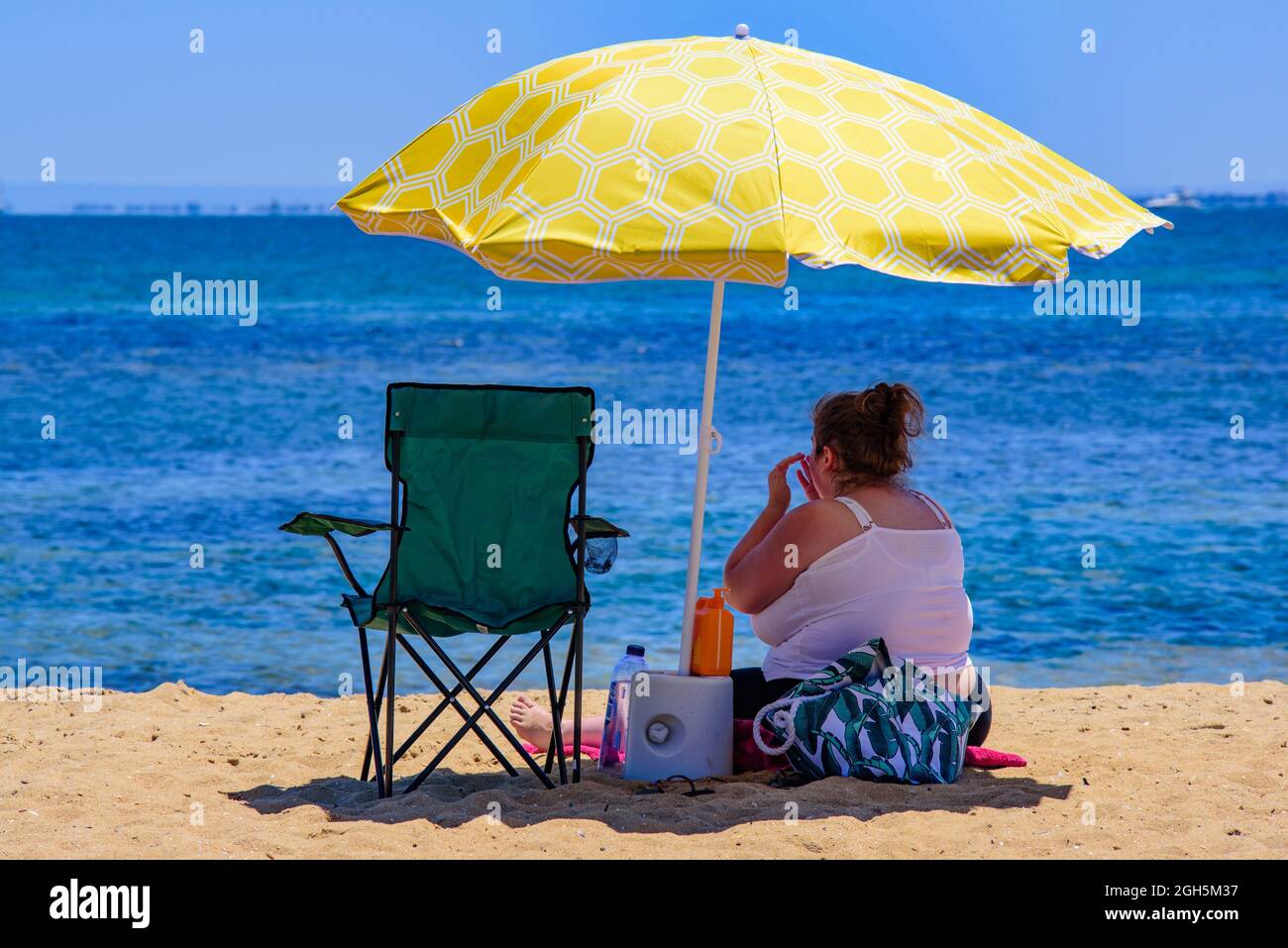 Eine übergewichtige Frau, die unter dem Sonnenschirm am Strand sitzt Stockfoto