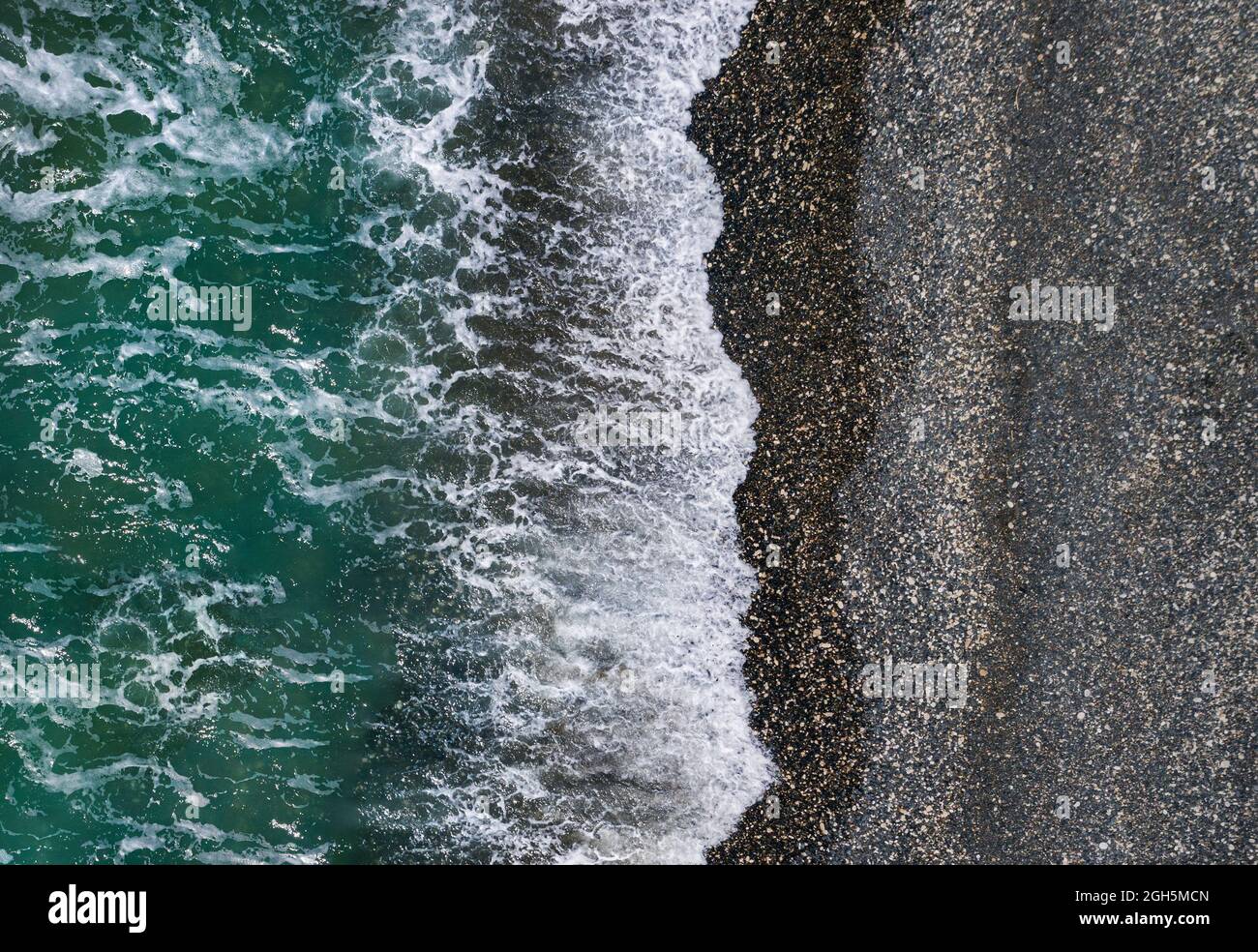 Grüne Meereswellen brechen auf schwarzem Sand und Kieselsteinen, Luft marine Textur Stockfoto