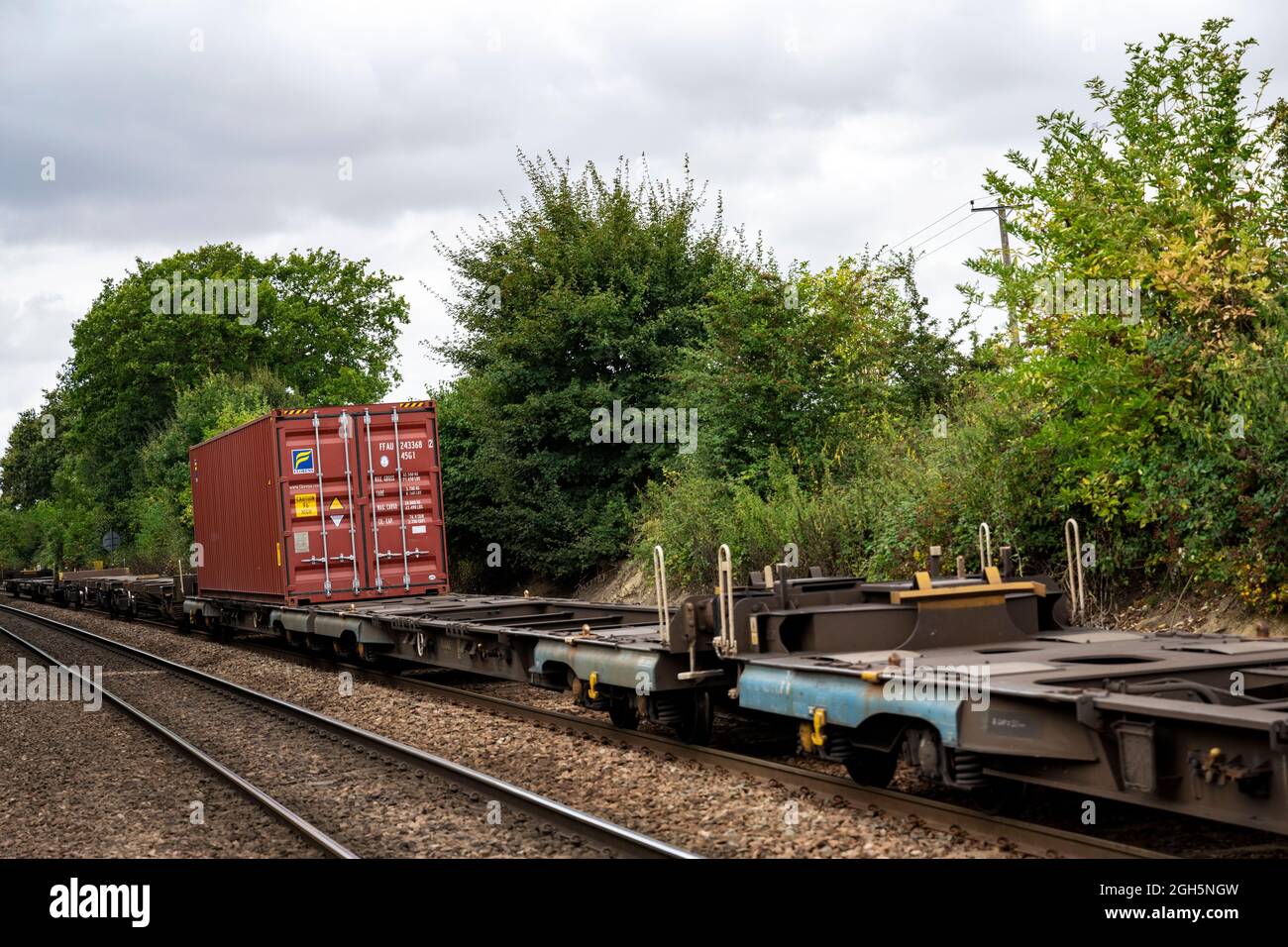 Ein Container auf meist leeren Flachbett-Eisenbahnwaggons in Richtung Hafen Felixstowe, Westerfield, Suffolk, Großbritannien. Stockfoto