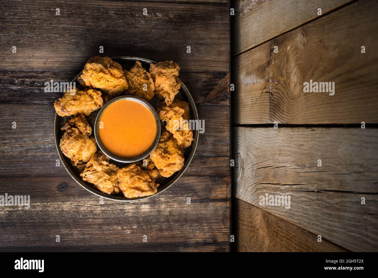 Von oben von leckeren frittierten knusprigen Huhn und Sauce auf runden Teller auf Holztisch in der Nähe der Wand serviert Stockfoto