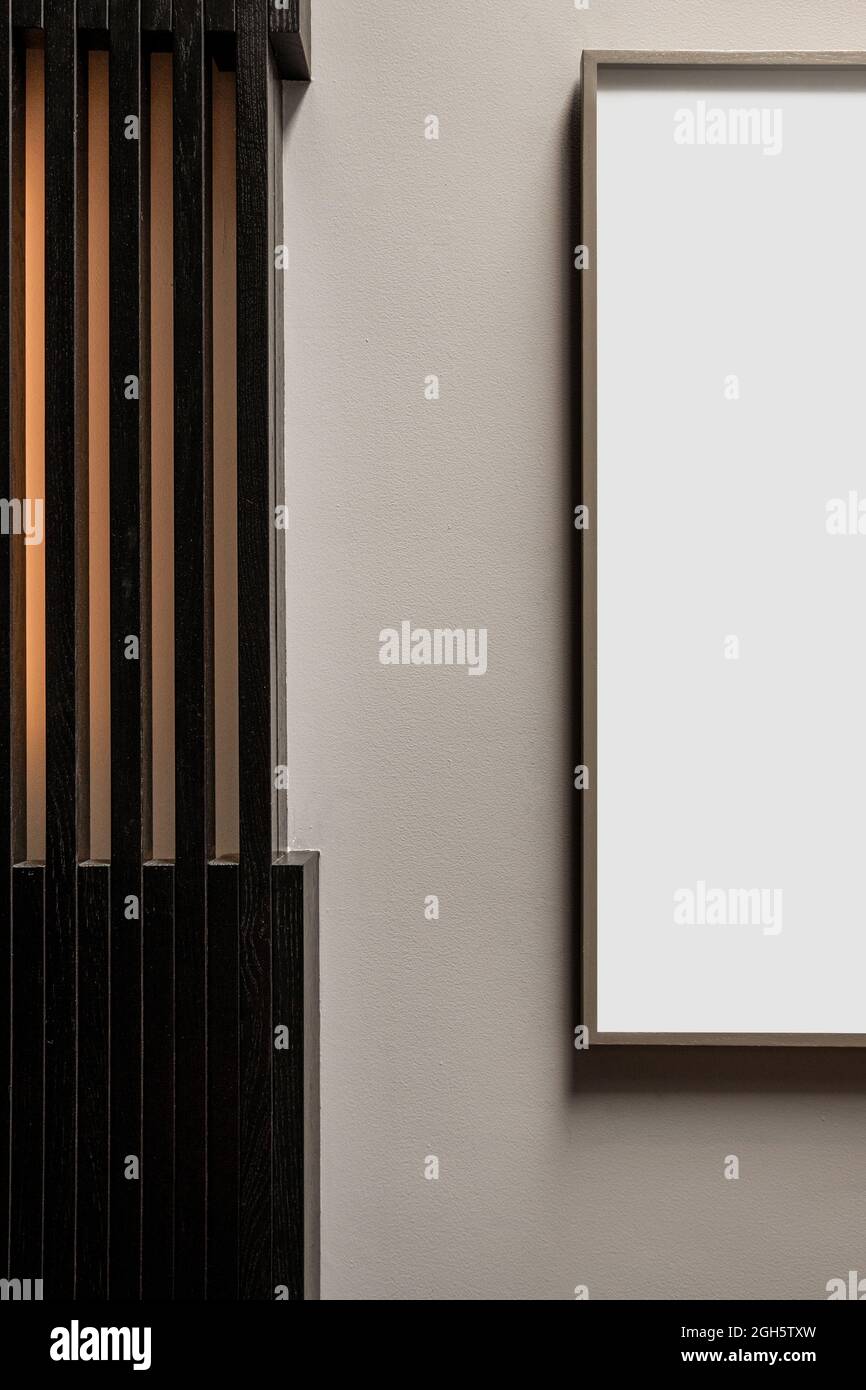 Fragment der Inneneinrichtung mit weißem rechteckigem Mockup-Rahmen, der an der Wand in der Nähe der gestreiften Säule hängt Stockfoto