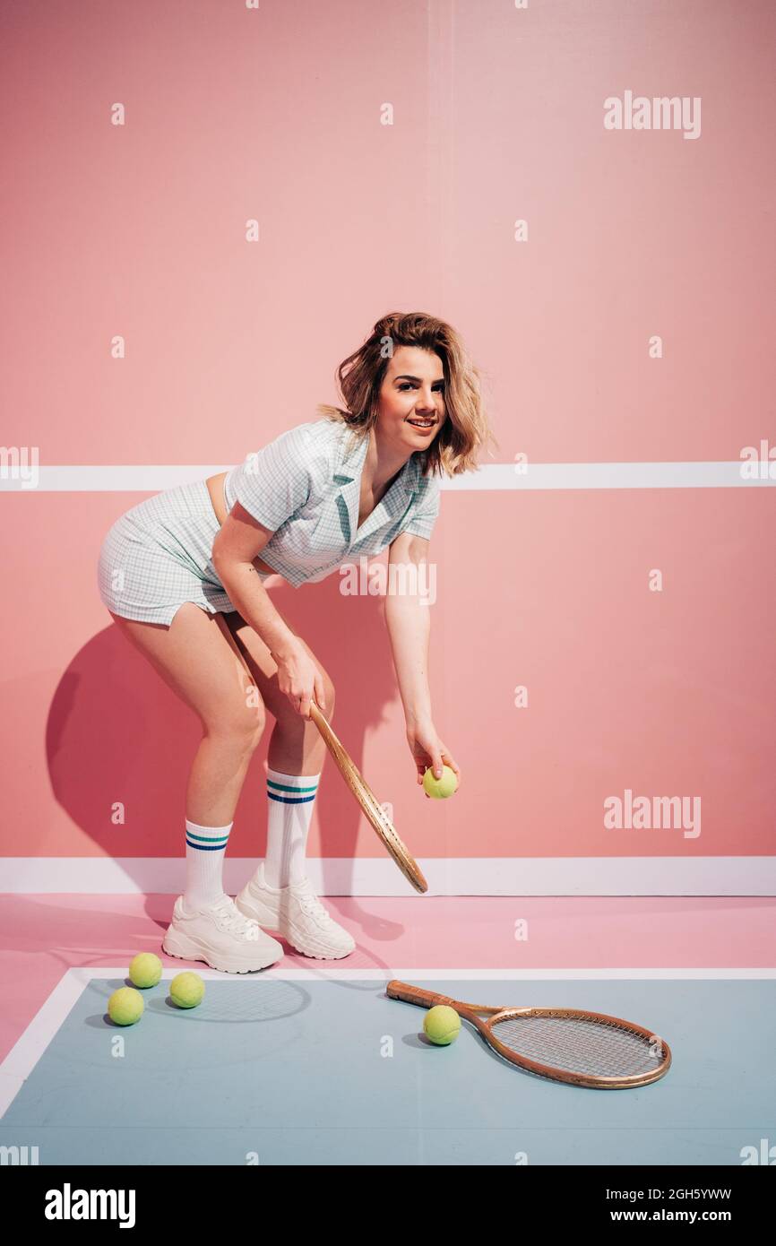 Seitenansicht einer fröhlichen jungen Sportlerin in Sneakers mit Tennisschläger, der auf dem Sportplatz die Kamera anschaut Stockfoto