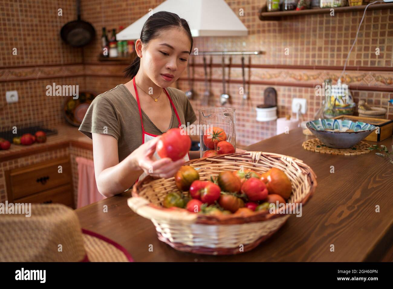 Fokussierte ethnische Hausfrau, die frische Tomaten in der Küche auswählt, während sie zu Hause kocht Stockfoto