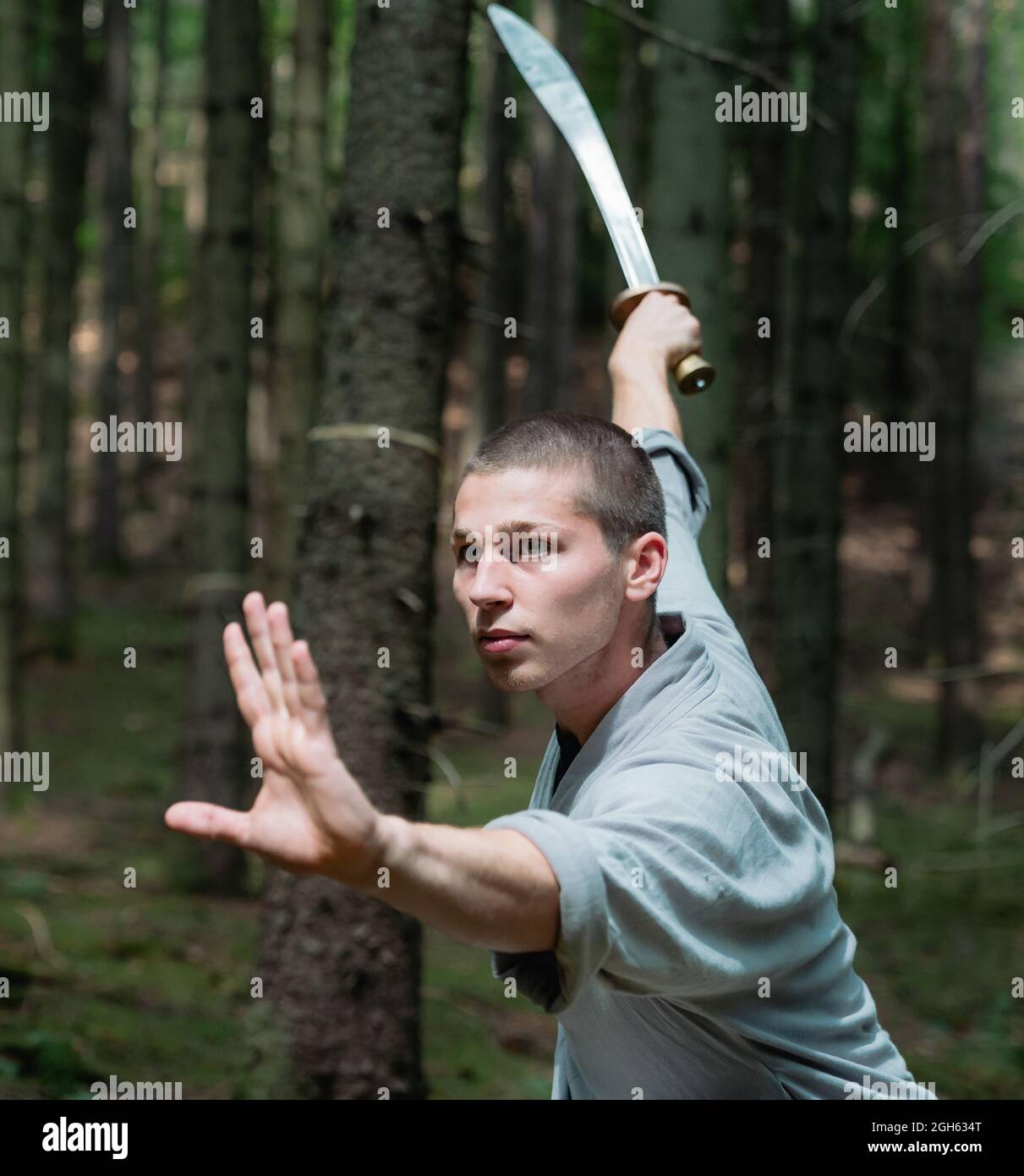 Der Mann in traditioneller Kleidung übt während des Kung Fu-Trainings im Wald die Schwerthalle Stockfoto