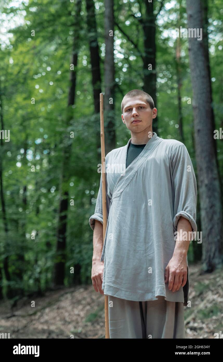 Mann, der die Hand in der Nähe der Brust hält, während er im Wald Kung Fu übt und dabei die Kamera anschaut Stockfoto