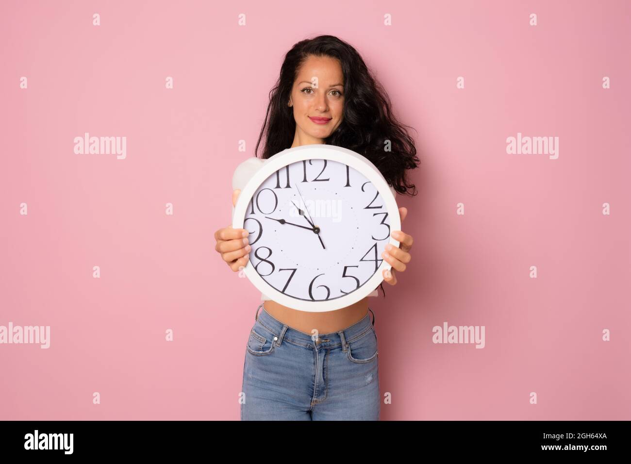 Junge schöne Frau hält eine große Uhr isoliert über rosa Hintergrund Stockfoto